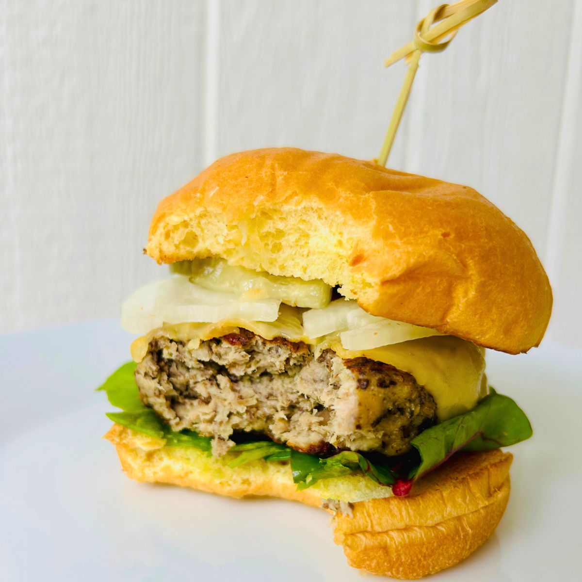 A partially eaten juicy turkey burger with mushrooms topped with cheese in a bun and a toothpick holding it together.