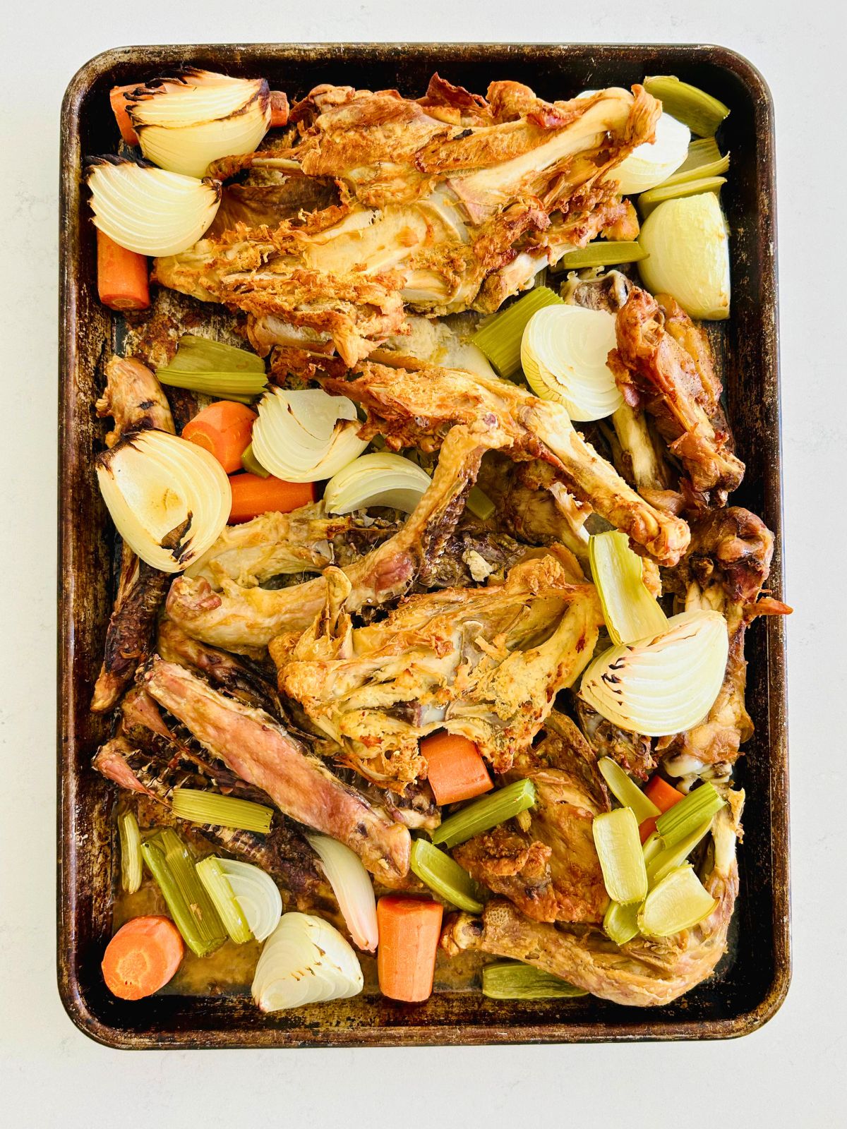 A sheet pan of roasted chicken bones, onions, celery, and carrots.