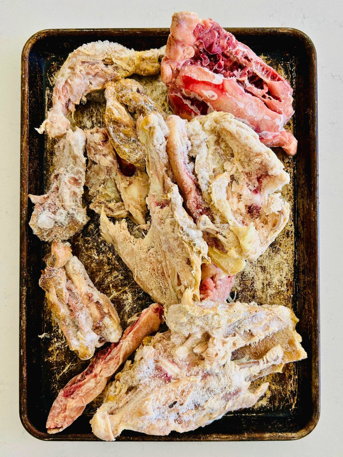Frozen chicken and turkey bones are on a cookie sheet ready to roast.
