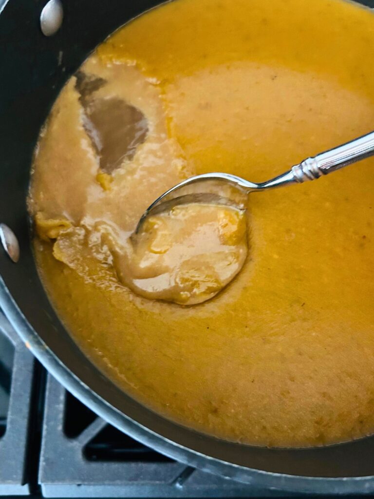 A spoon is used to scrape off the congealed fat from a pot of chilled brown chicken stock.