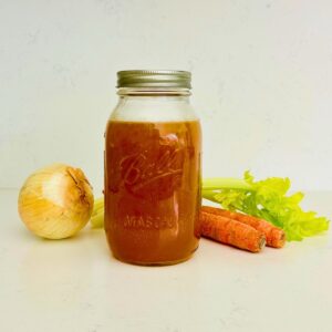 Brown chicken stock in a quart-sized mason jar next to carrots, celery, and onion.