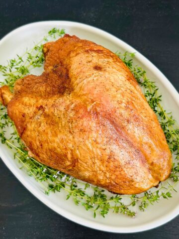 Oven roasted turkey breast with dry brine on a white oval platter with fresh thyme sprigs.