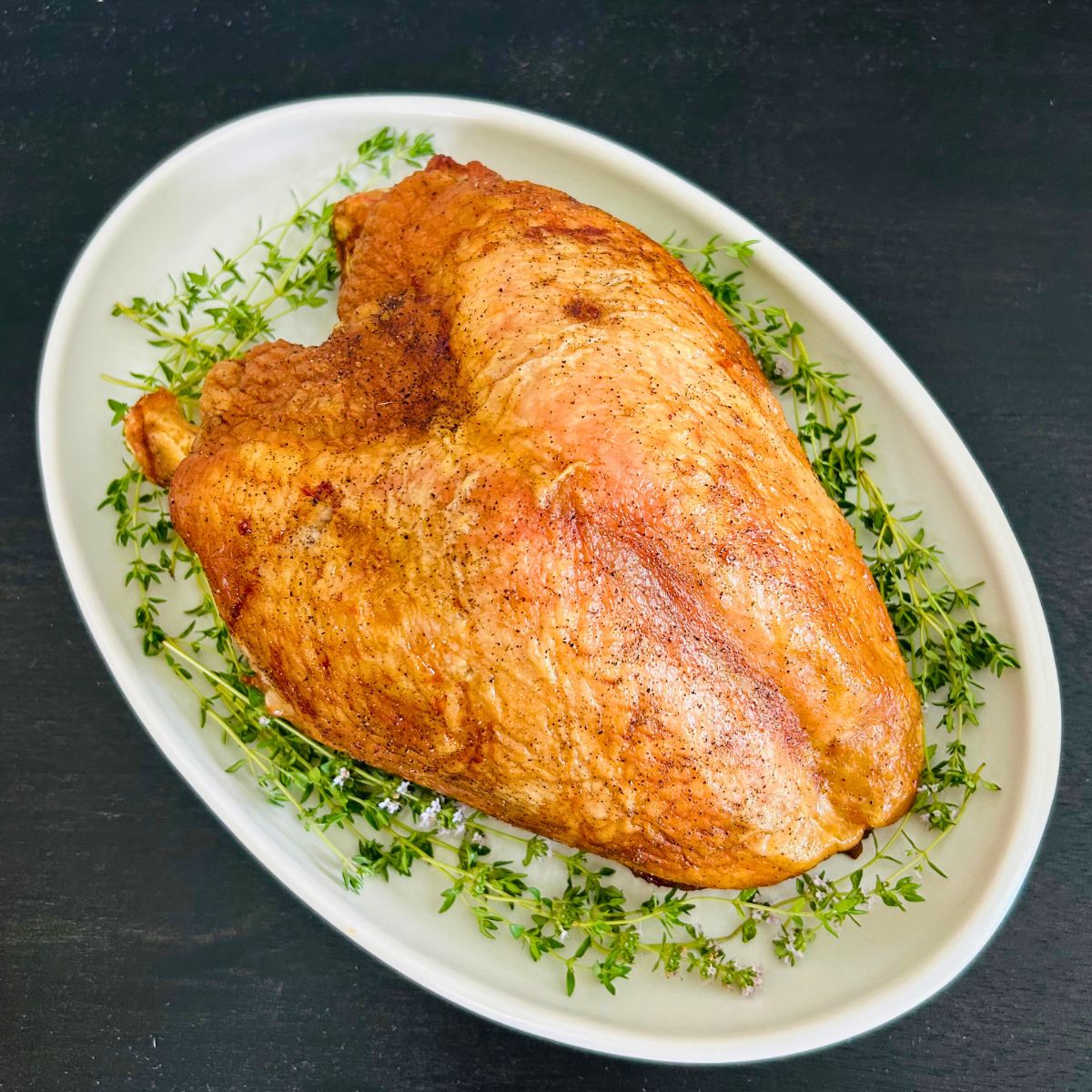 Oven roasted turkey breast with dry brine on a white oval platter with fresh thyme sprigs.