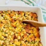 Stuffing recipe with two breads in a white casserole dish with a wooden spoon ready to scoop a serving.