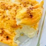 A serving is held in a spoon over the mashed potato casserole with cream cheese.