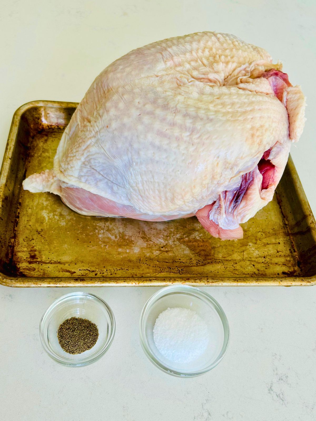A bone-in, skin on turkey breast next to bowls of salt and pepper.