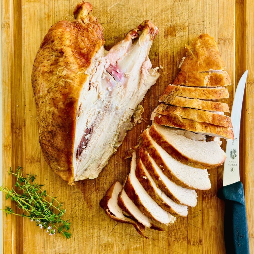 Carving a turkey breast into slices resting on a cutting board.