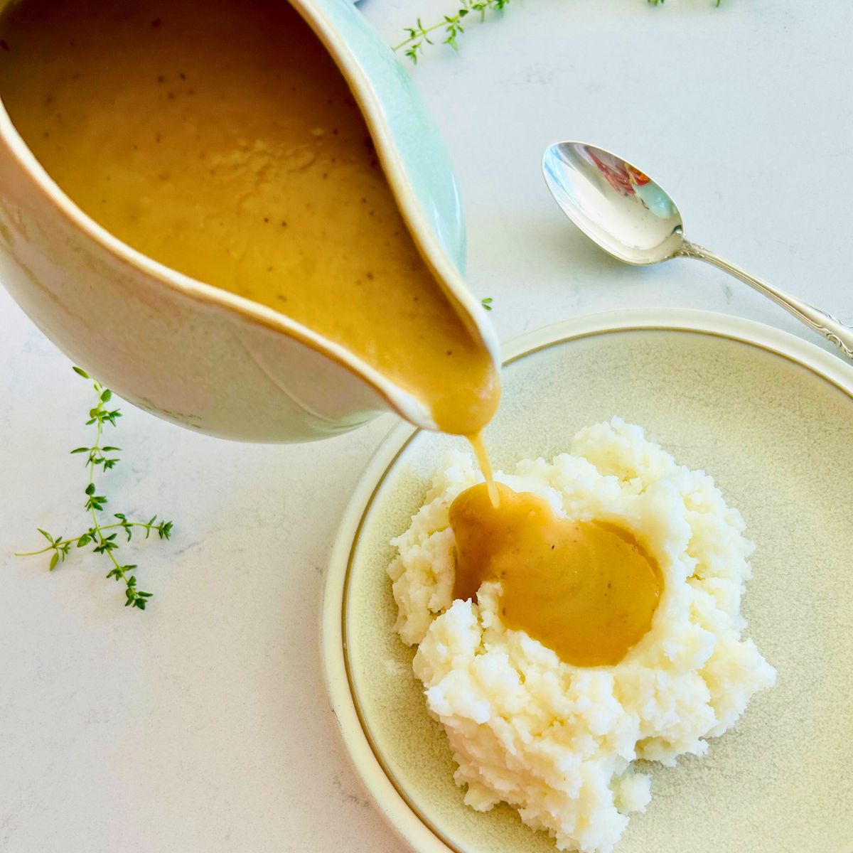 A gravy boat pouring turkey gravy without drippings over a plate of mashed potatoes.
