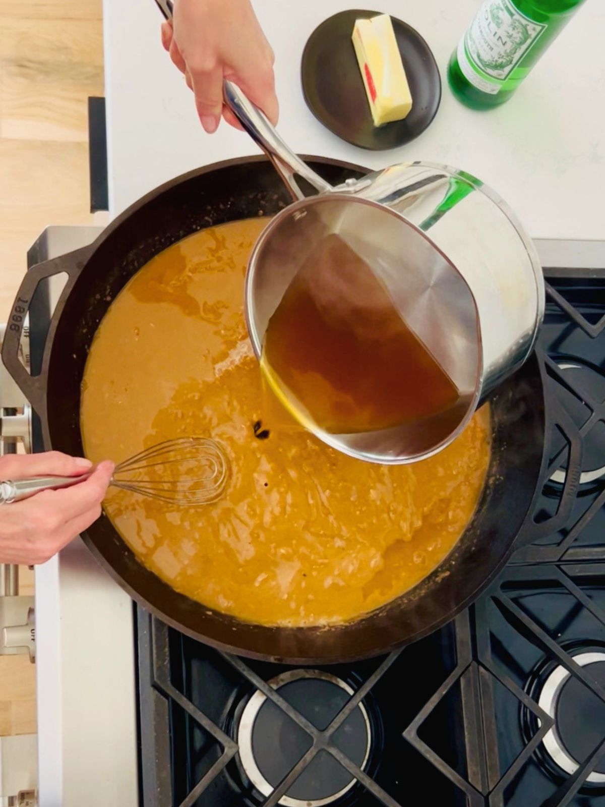 Homemade brown chicken stock is whisked into the cast iron skillet of turkey gravy.