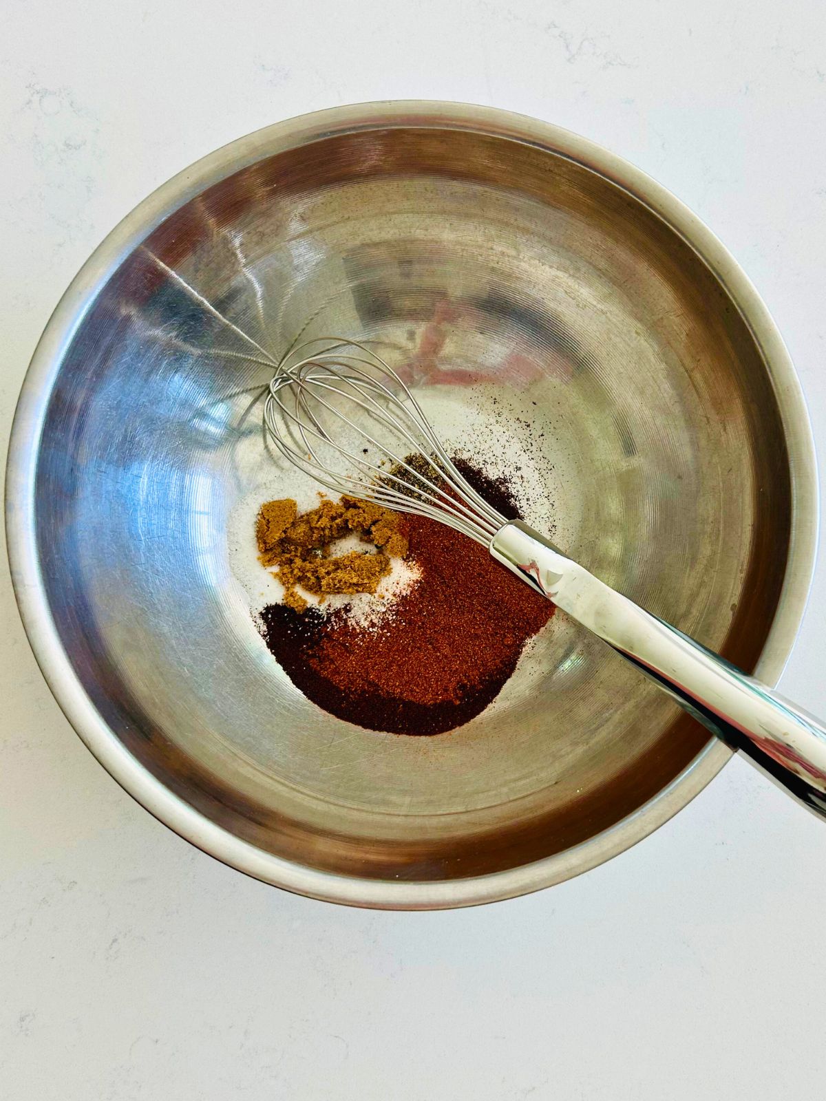 All of the spices to make an espresso rub in a metal bowl with a whisk.