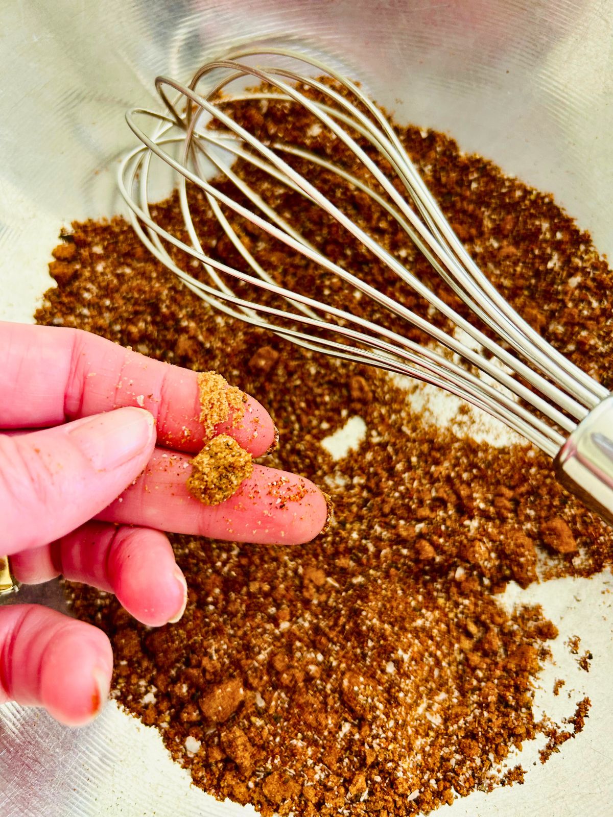 Small clumps of brown sugar are pinched between 2 fingers above a bowl of coffee rub.
