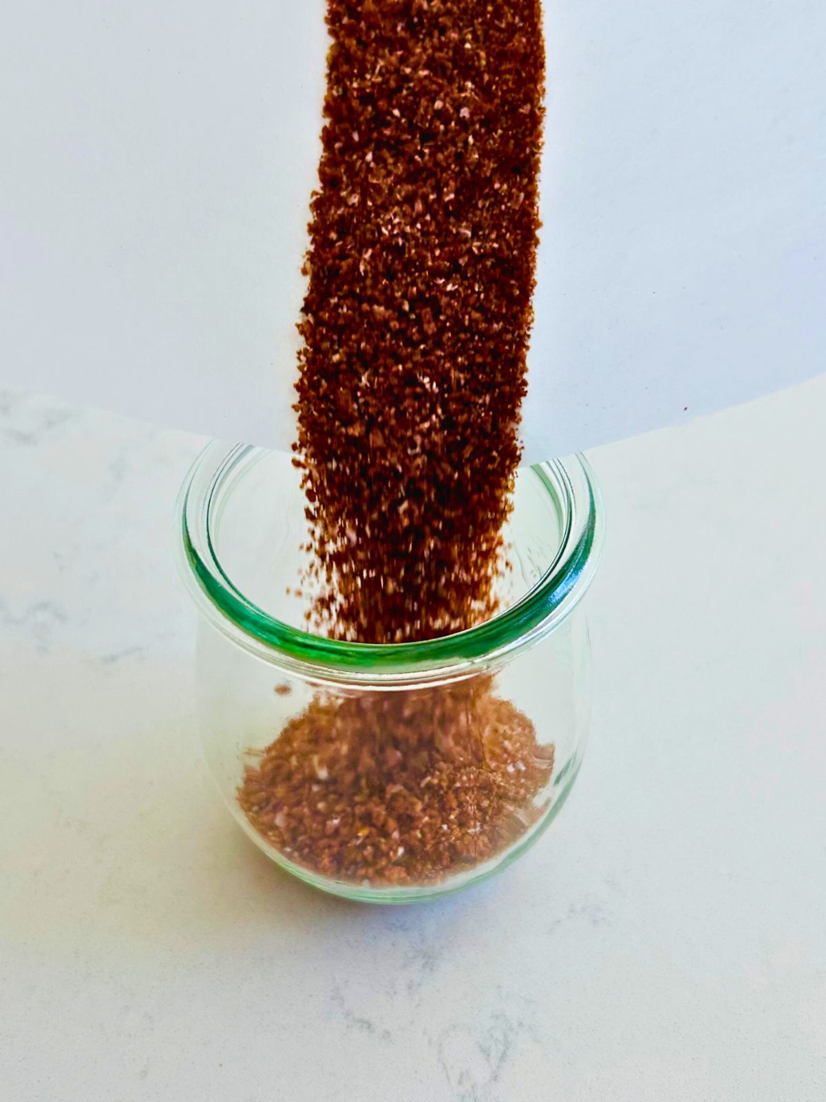 Parchment paper is used as a funnel to fill a small mason jar with espresso rub.