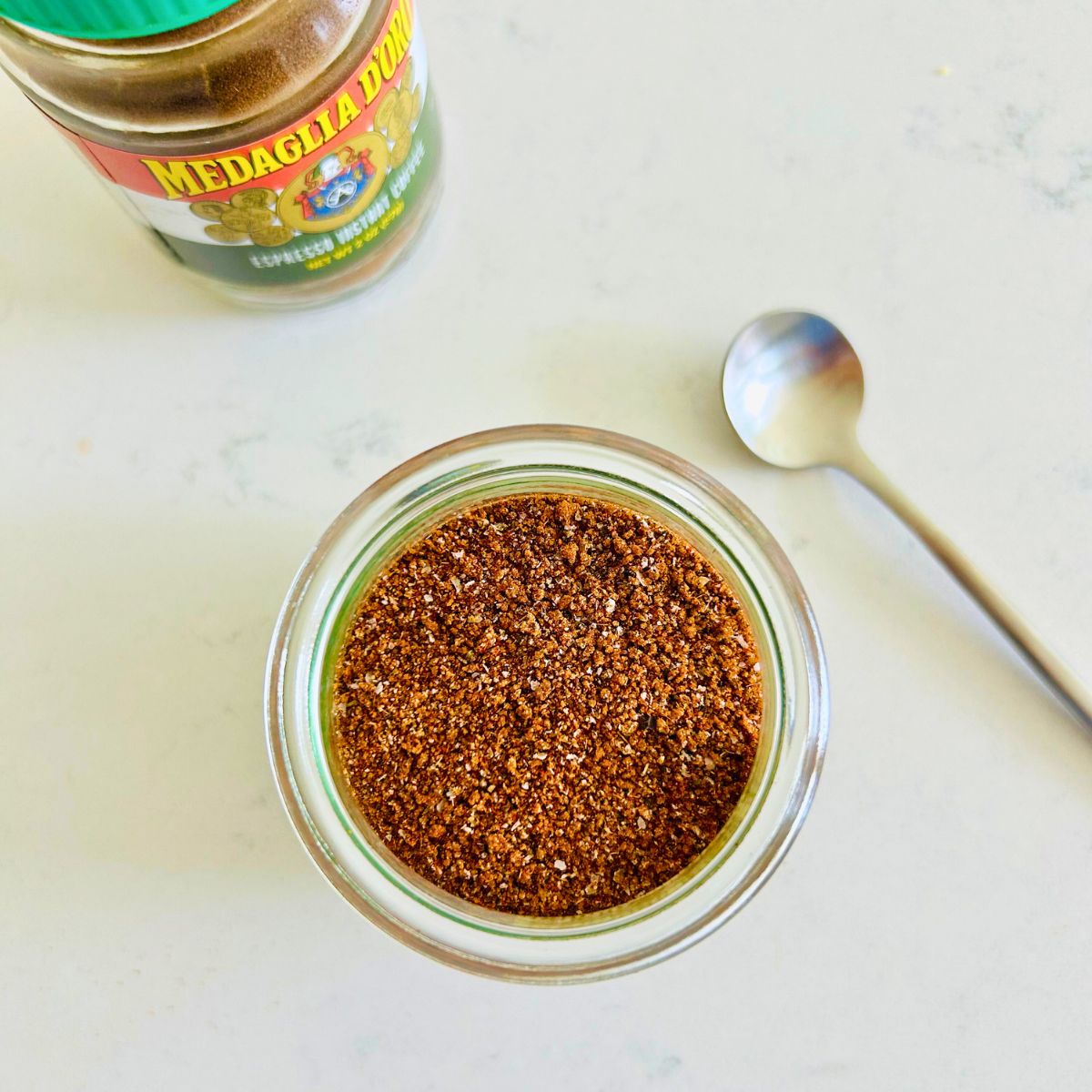 Espresso rub in a small mason jar next to a spoon and jar of instant espresso powder.