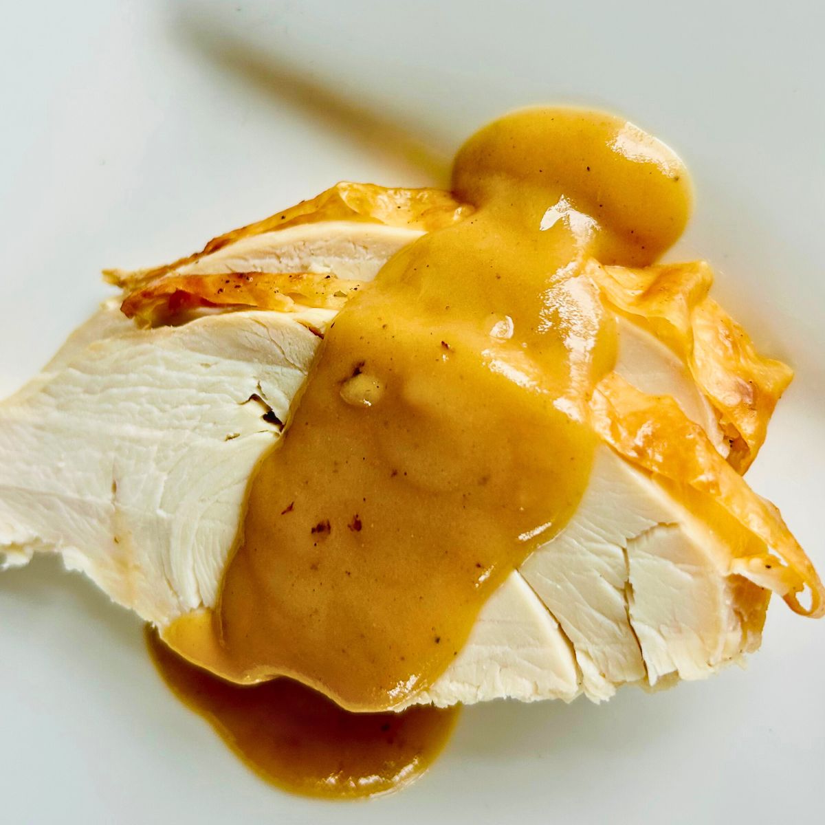 Sliced whole roasted turkey on a white plate with pan gravy spooned over it.
