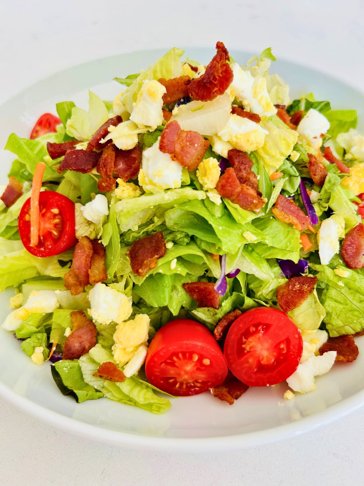 Houston's salad with bacon crumbles and chopped hard boiled eggs in a white bowl.