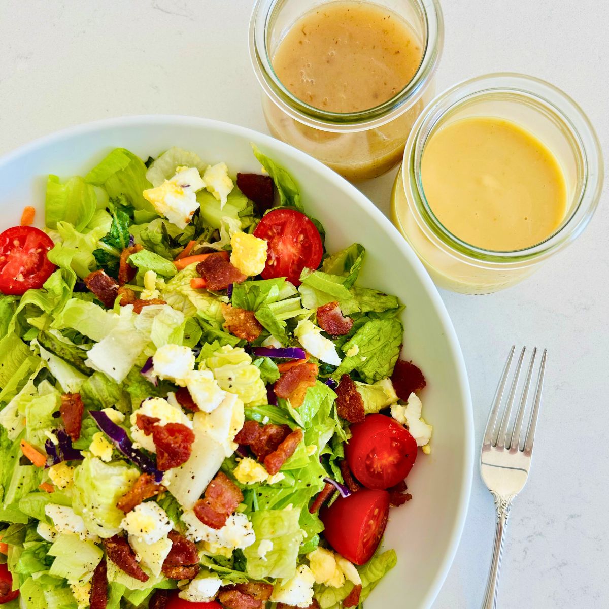 Houston’s salad with cups of hot bacon and honey mustard in a white bowl next to a fork.