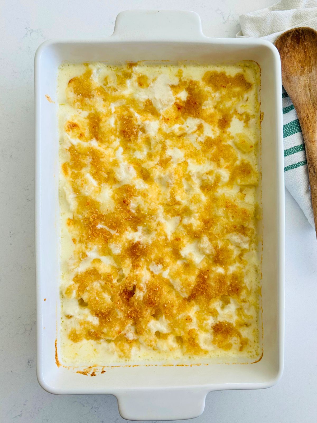 A hot white casserole of steakhouse potatoes au gratin next to a wooden spoon.