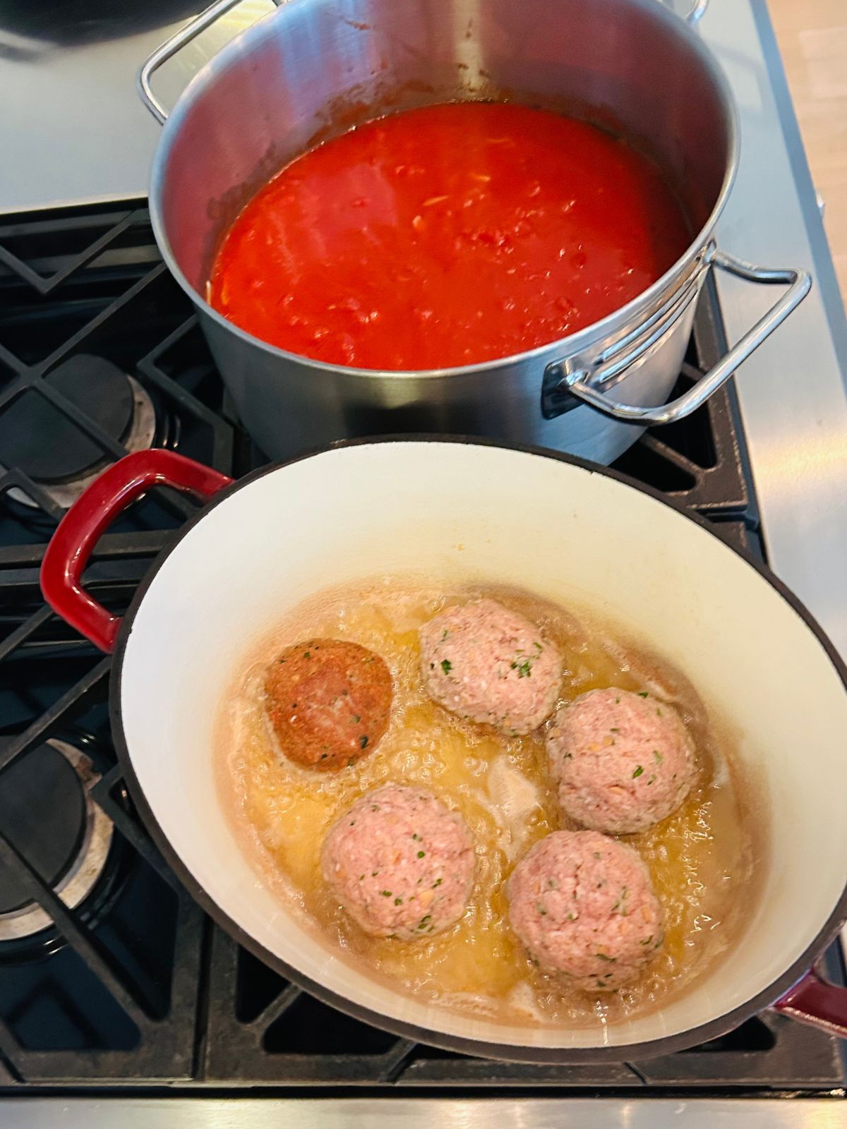Italian meatballs are pan frying next to a pot of marinara sauce.
