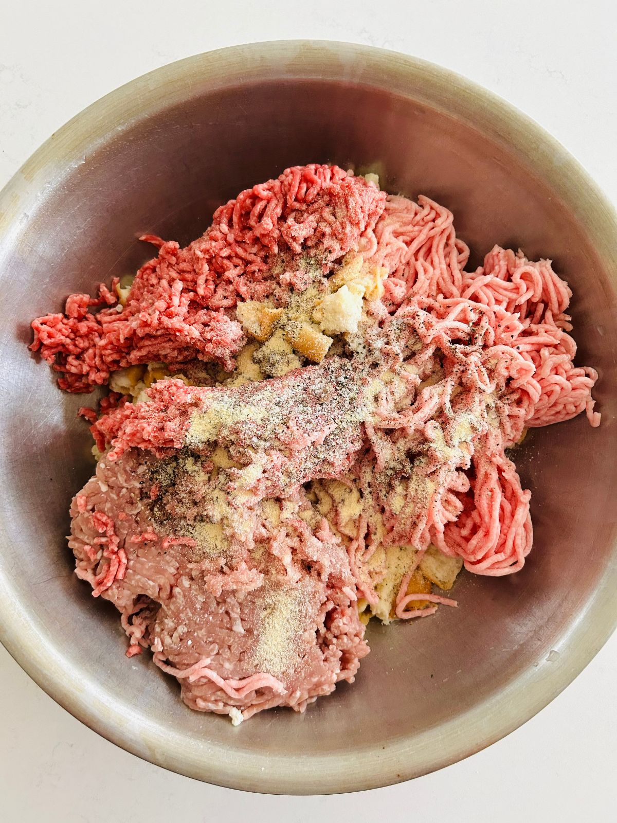 A bowl of ground beef, pork, and veal in a bowl with seasonings and panade.