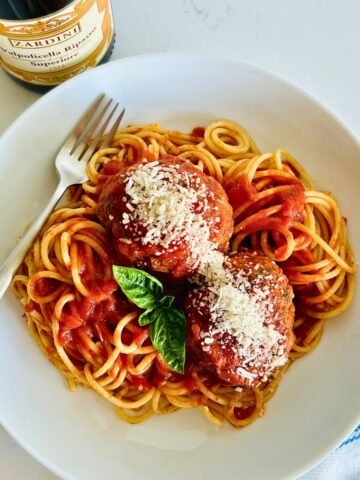 The best Italian meatballs recipe (Cafe Martorano copycat) in a white bowl with a fork next to a bottle of red wine.