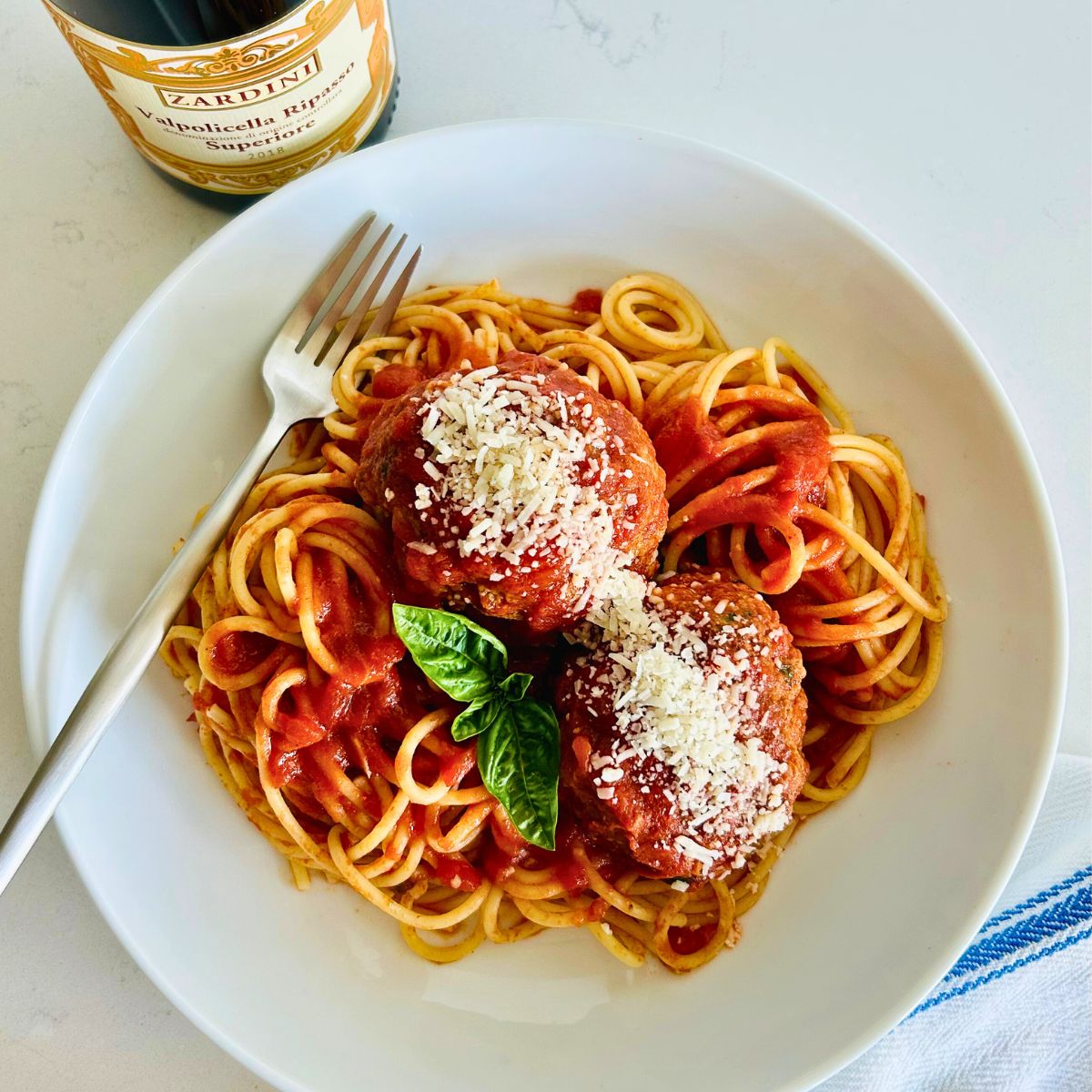 The best Italian meatballs recipe (Cafe Martorano copycat) in a white bowl with a fork next to a bottle of red wine.