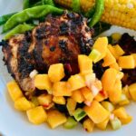 Grilled chicken thighs with peach salsa on a white plate.