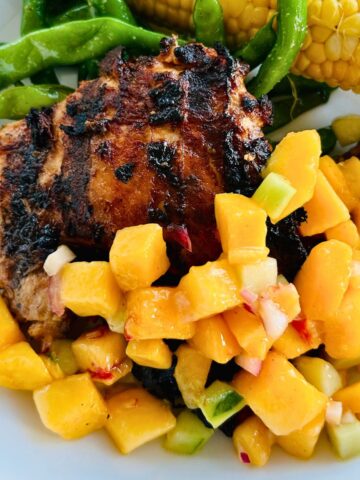 Grilled chicken thighs with peach salsa on a white plate.