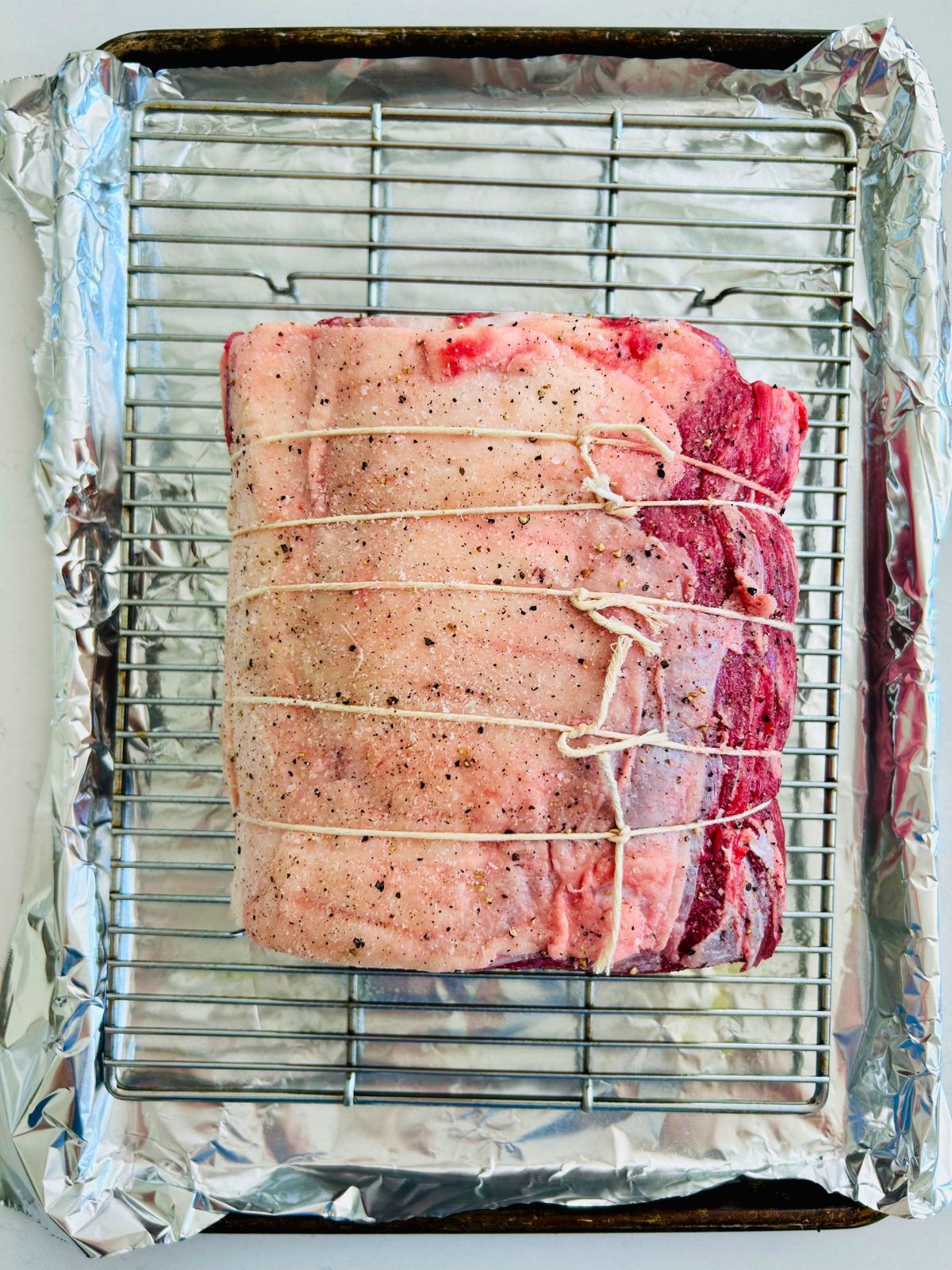 Seasoned slow roasted prime rib on a rack over a sheet pan.