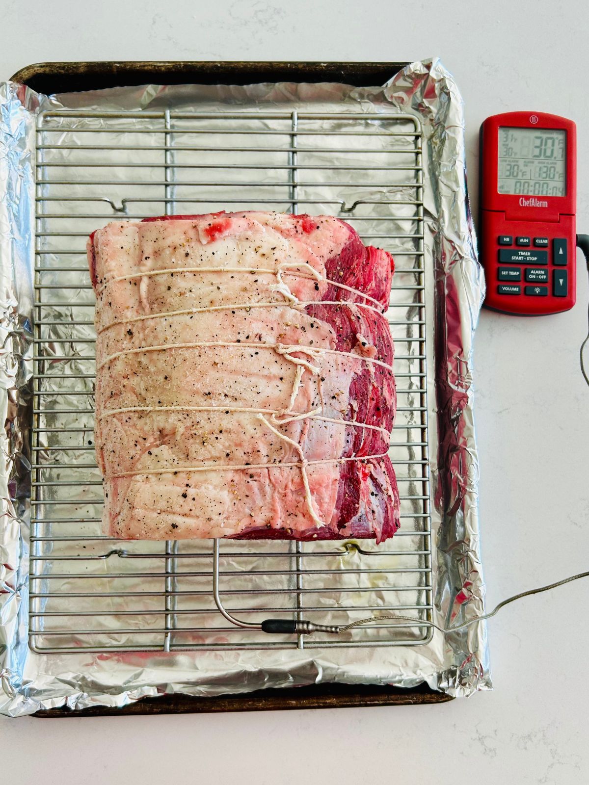 A seasoned prime rib roast tied with butcher string with a thermometer probe inserted ready to roast.