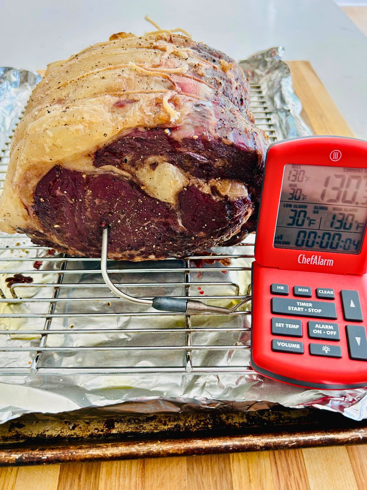 A prime rib roast has been slow roasted with a thermometer probe inserted into it showing an internal temperature of 130°F.