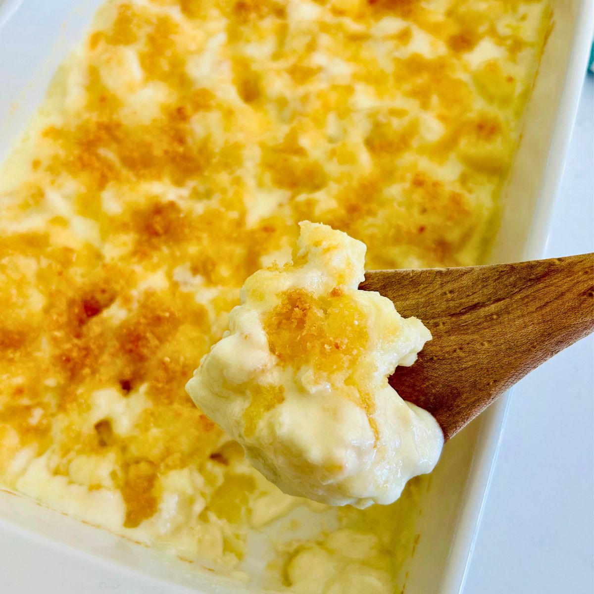 Steakhouse potatoes au gratin in a casserole dish with a wooden spoon holding a serving.