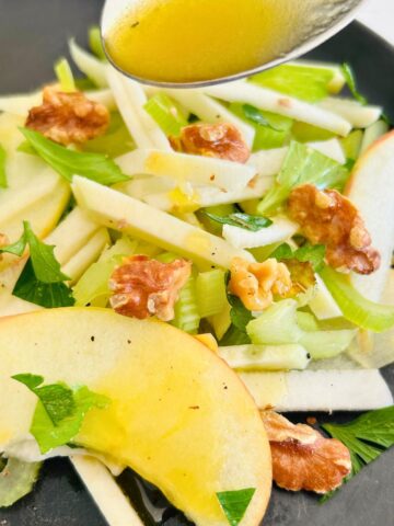 Apple kohlrabi salad with toasted walnuts and celery getting dressed with a spoon of apple cider vinaigrette.