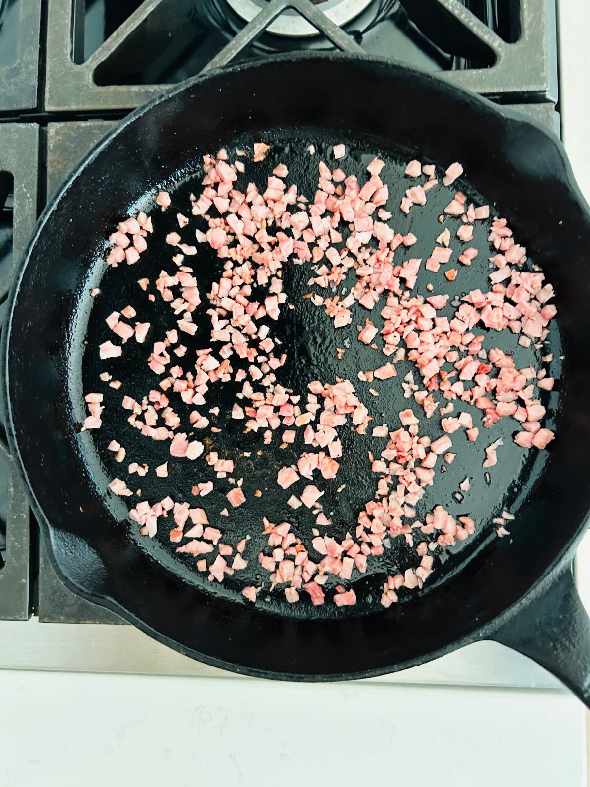 Sautéed ham bits in a cast-iron skillet over a burner.