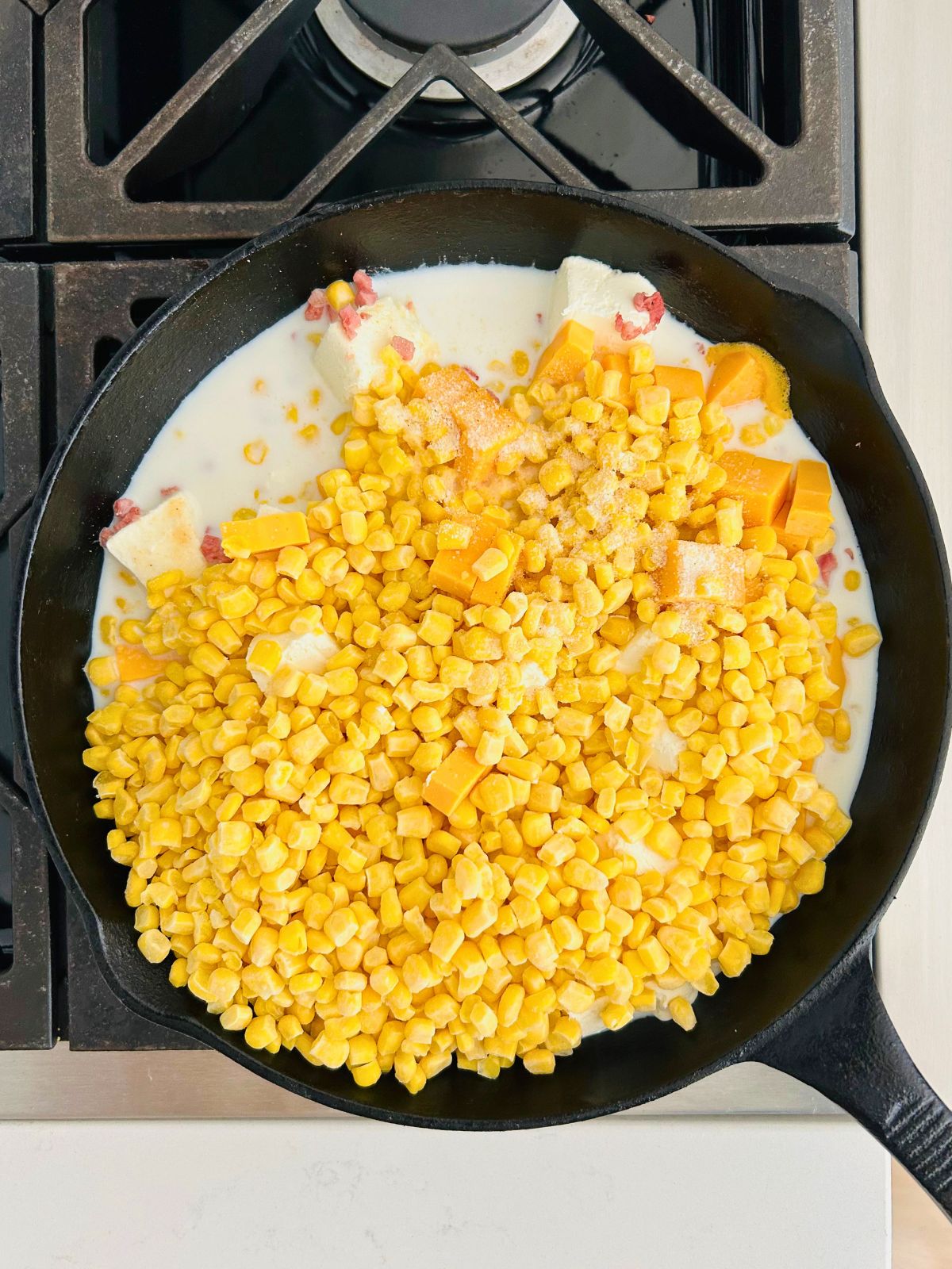 Cheese cubes, milk, ham, and frozen corn kernels in a skillet on the stove.