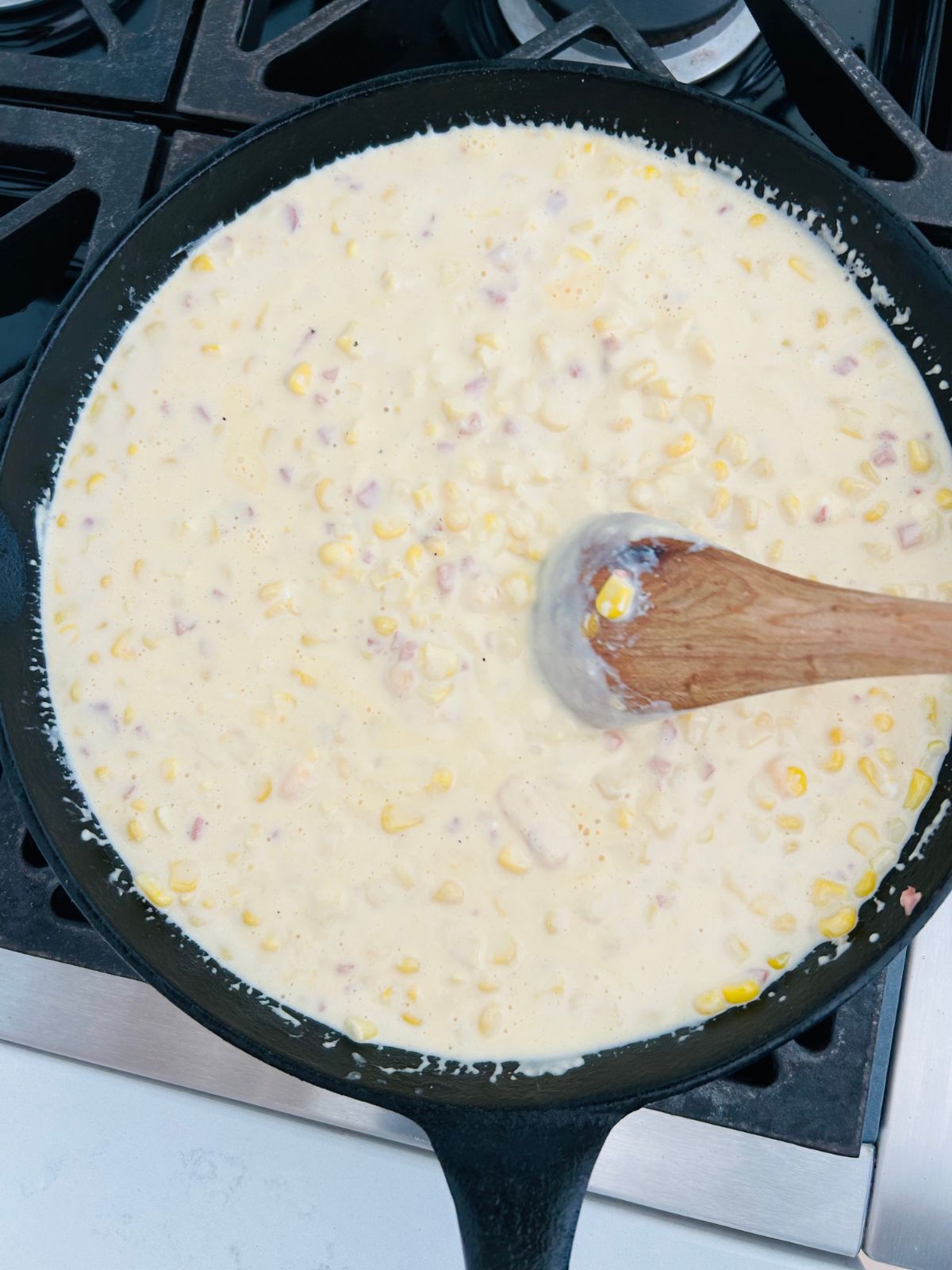 Stirring and melting the ingredients for cheesy corn bake in a skillet on the stovetop.