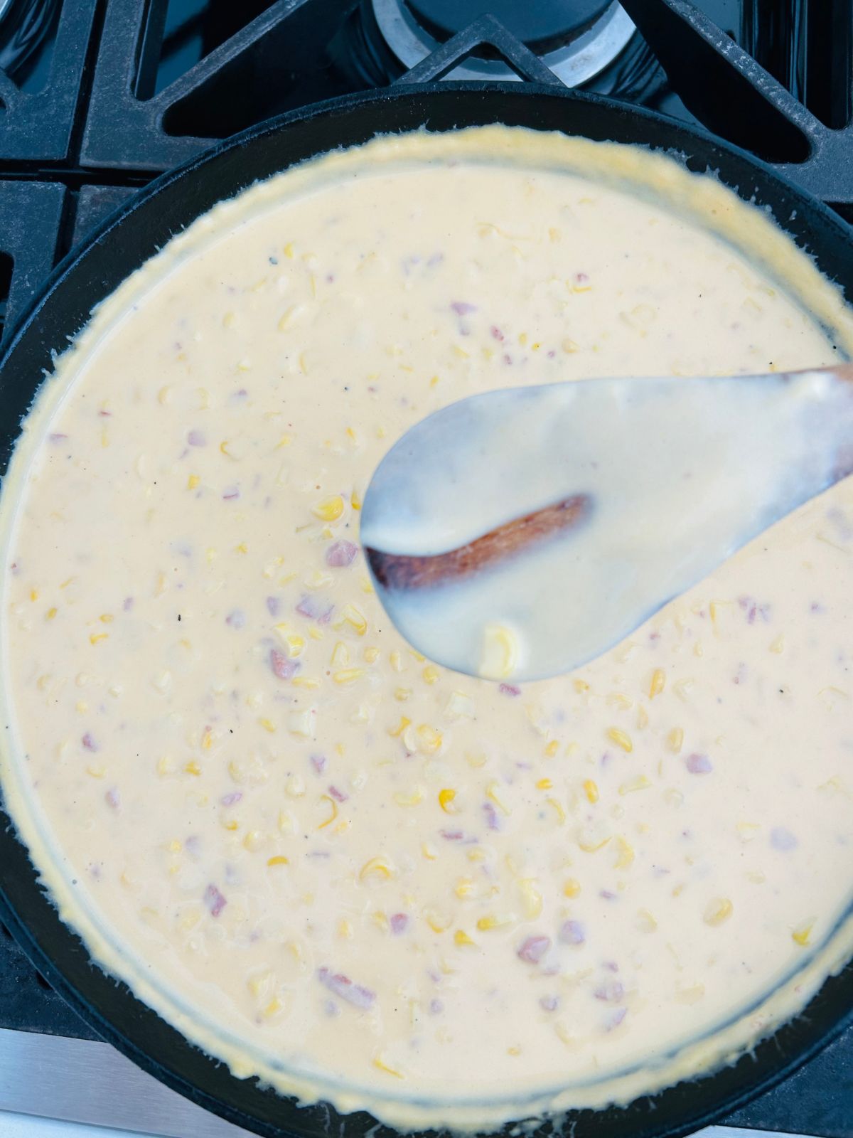 Jack Stack cheesy corn recipe with a wooden spoon dipped in the cheese sauce that shows a trail from a finger wiped down the spoon.