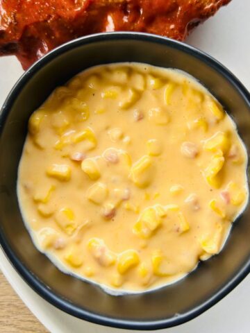 Jack Stack cheesy corn recipe in a black bowl next to a barbecue rib.