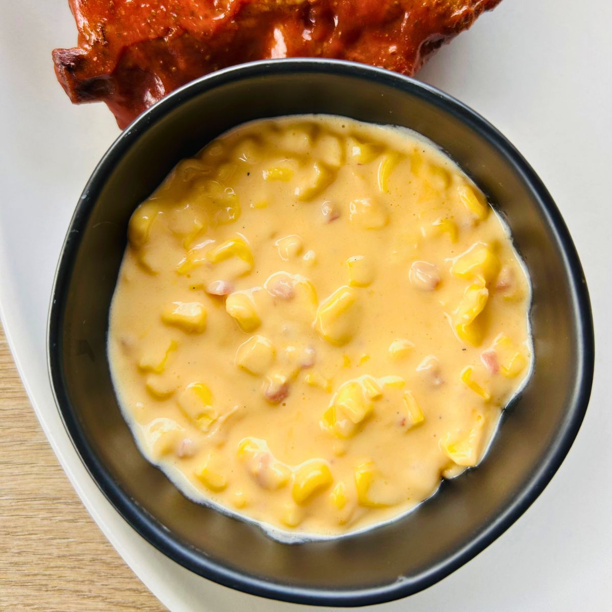 Jack Stack cheesy corn recipe in a black bowl next to a barbecue rib.