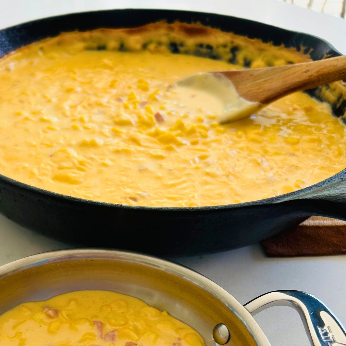 A cast iron skillet of Jack Stack cheesy corn recipe with a wooden spoon.