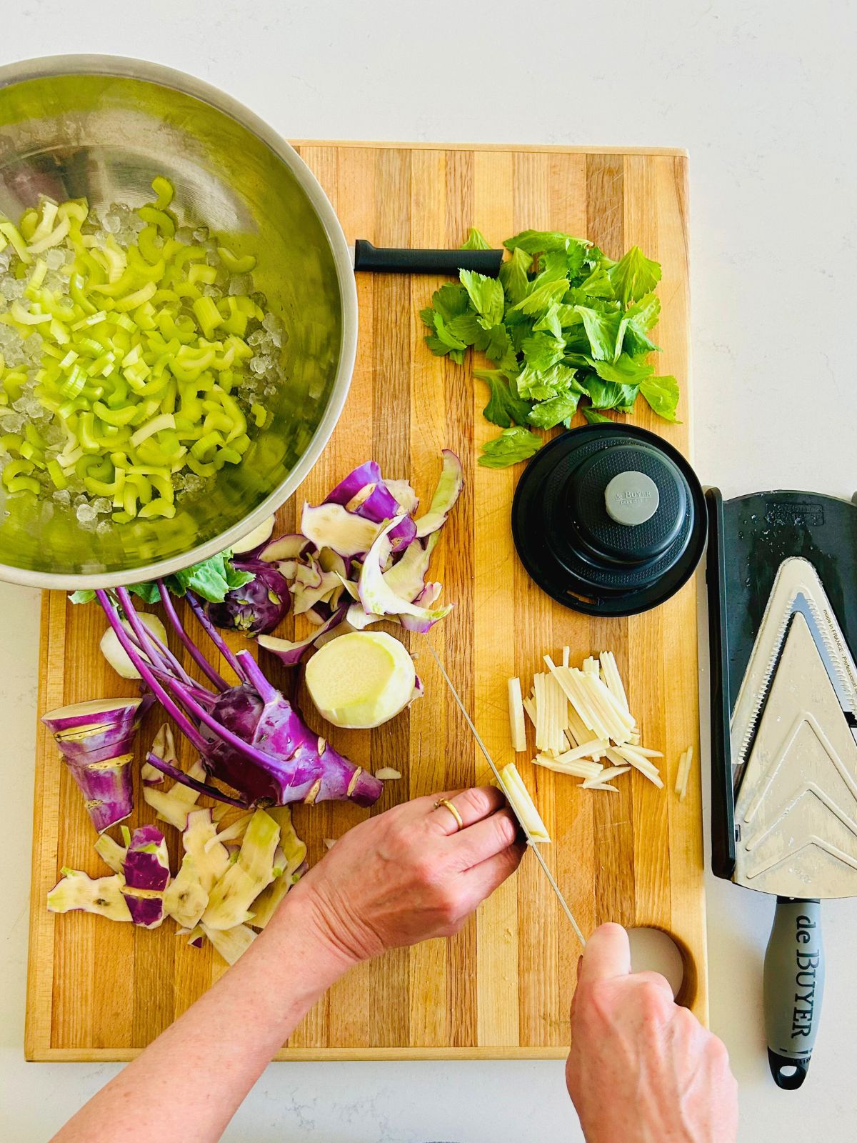 Kohlrabi is peeled, sliced, and julienned with a chef's knife next to an ice bowl of sliced celery.