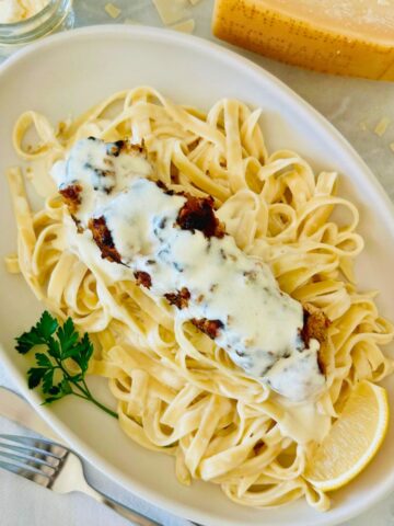 Garozzo's Ristorante copycat chicken spiedini recipe on a white oval plate next to parmesan cheese, fork, and a napkin.