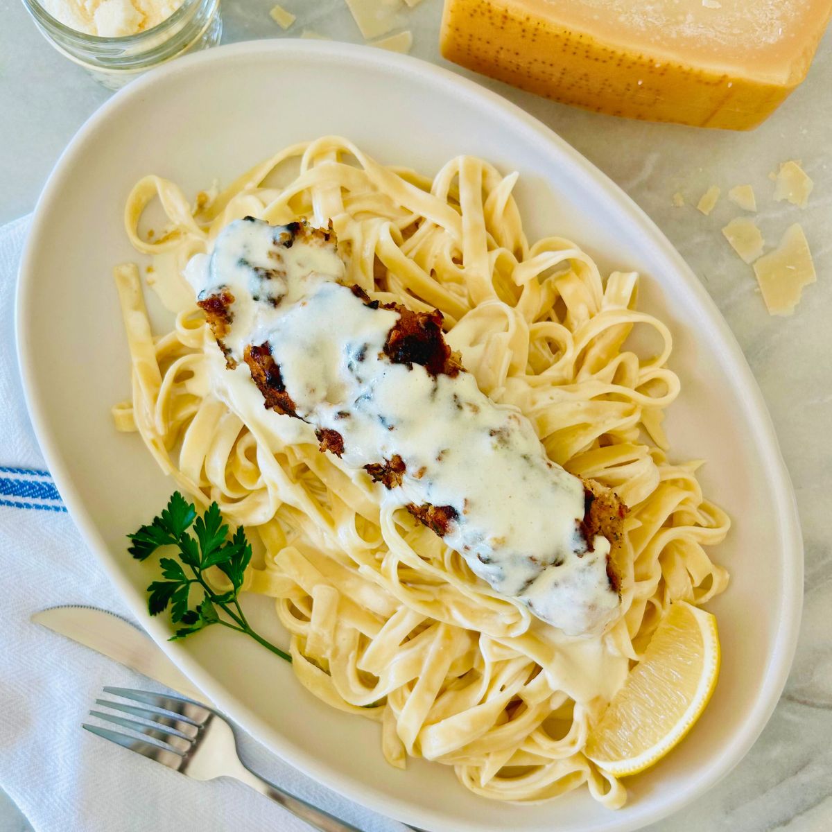 Garozzo's Ristorante copycat chicken spiedini recipe on a white oval plate next to parmesan cheese, fork, and a napkin.