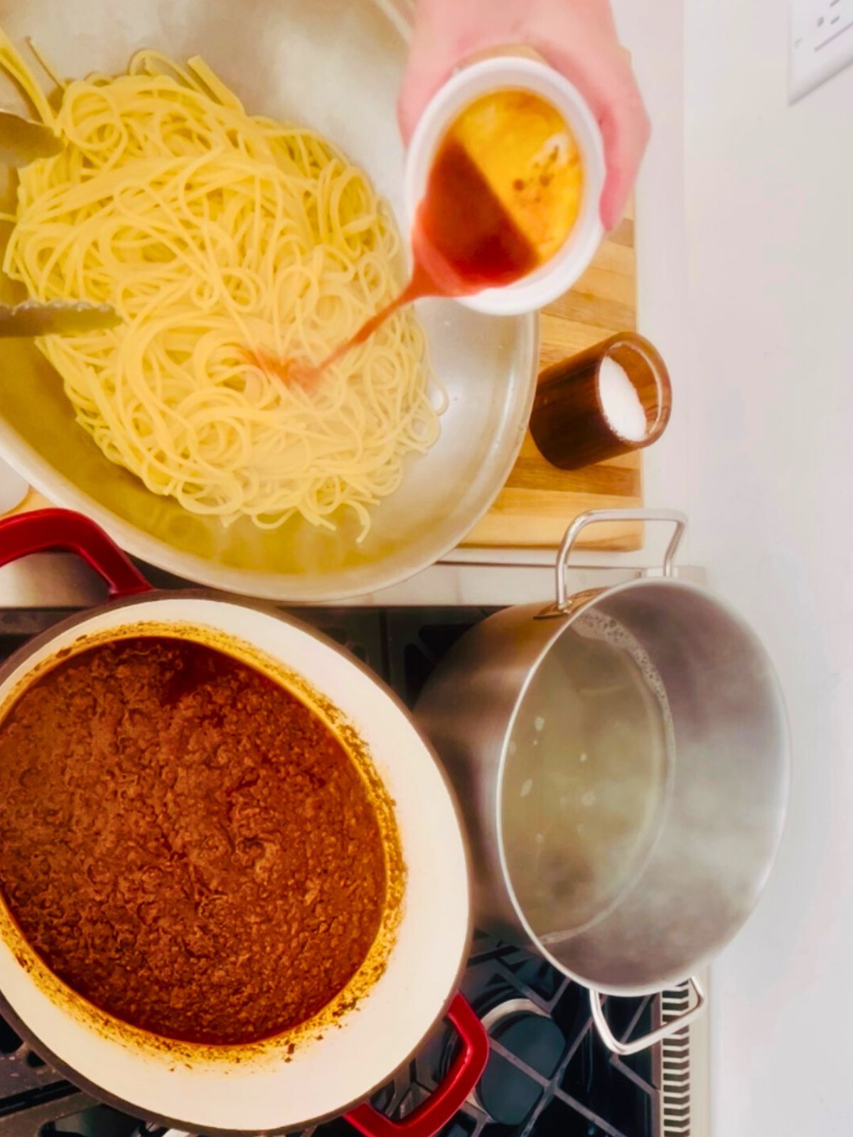 Chili-stained hamburger fat is poured over cooked spaghetti next to a pot of Fred and Red-style chili.