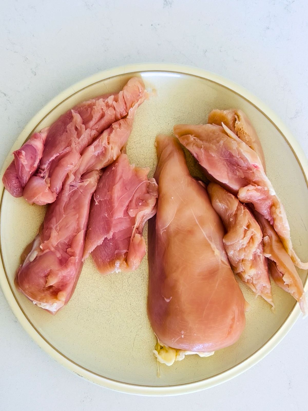 Boneless, skinless chicken breasts are cut into thirds and resting next to a whole breast on a white plate.