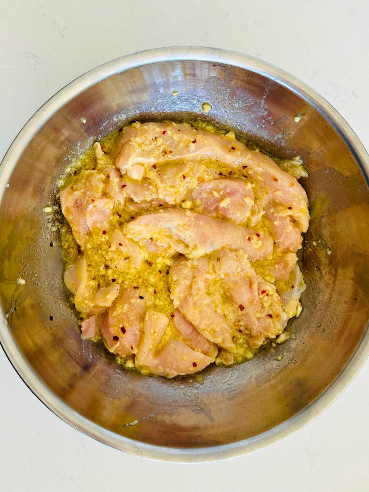Pieces of chicken breasts for chicken spiedini are marinating in a bowl of lemon, olive oil, garlic, and red pepper.