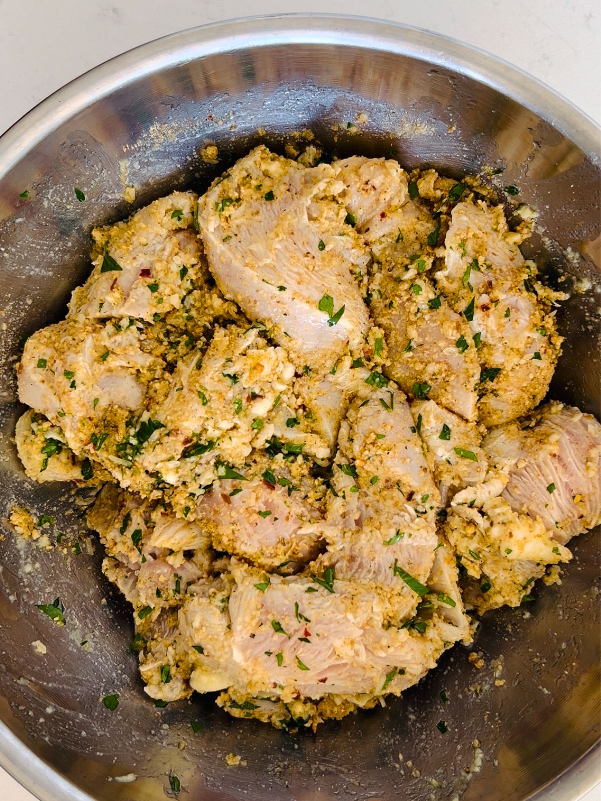 Marinated and breaded pieces of chicken spiedini in a mixing bowl.