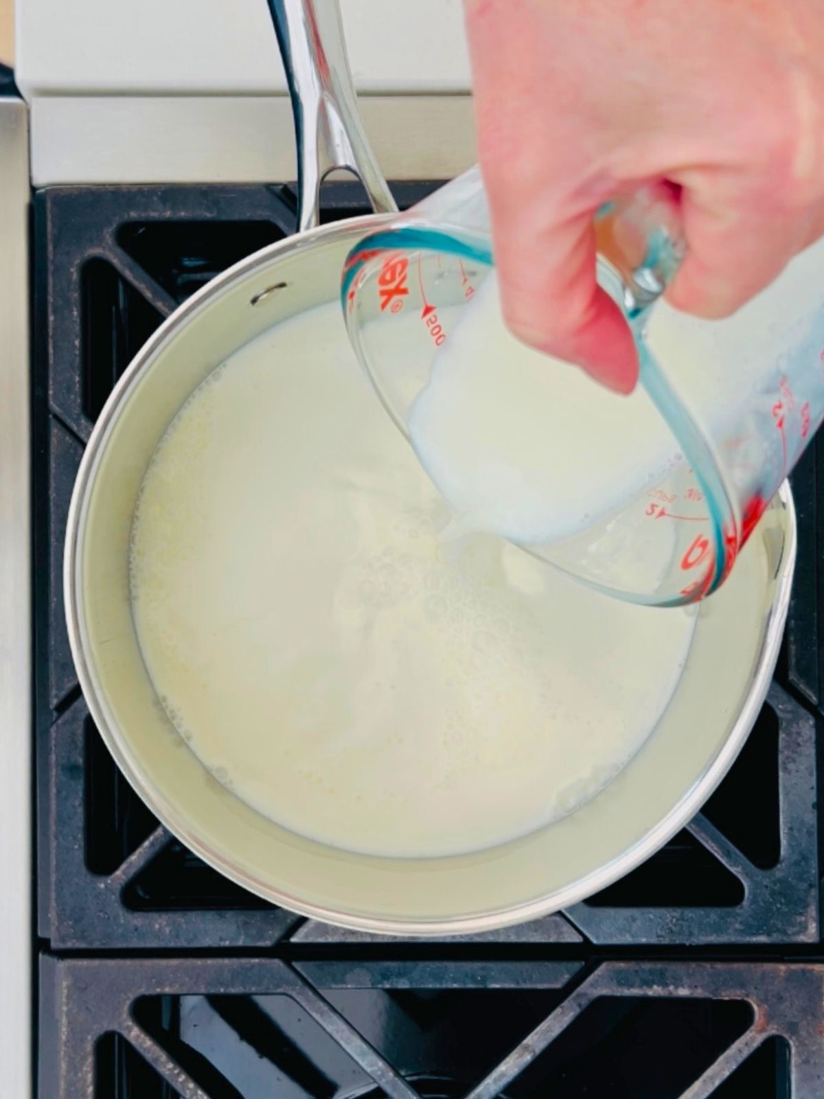 Cream is poured into a saucepan over a stove's burner.