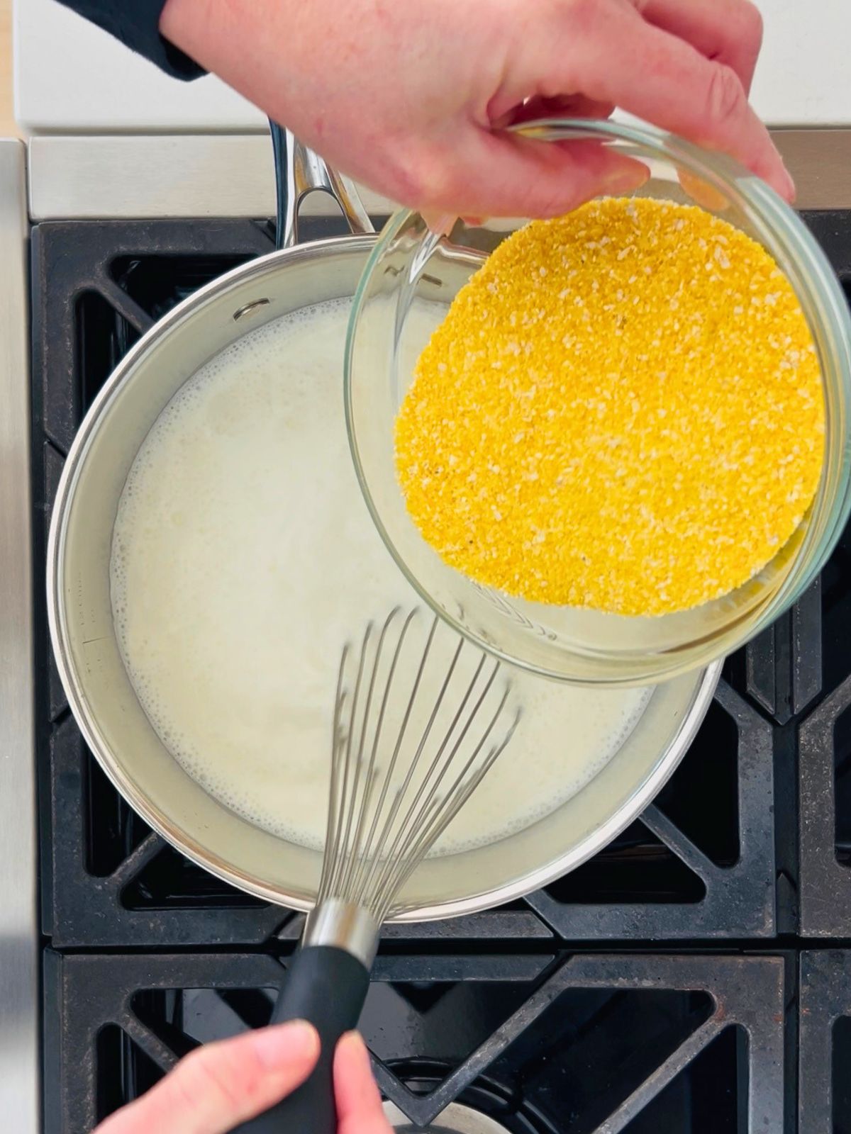 Whisking dried polenta into hot milk and cream in a saucepan.