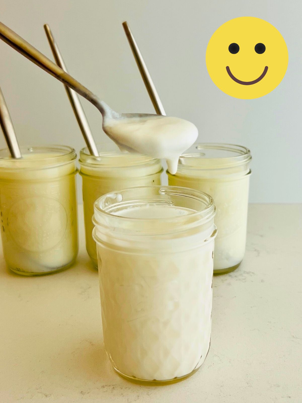 A successful batch of cultured buttermilk with a spoonful of thick buttermilk held over a mason jar.