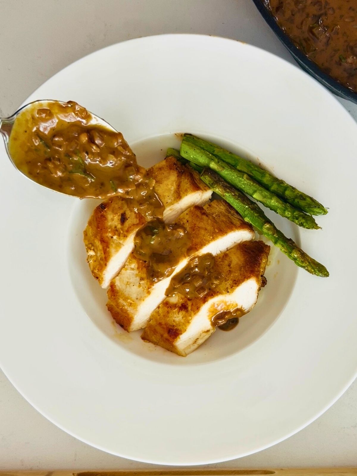 Pan-seared chicken breast, sliced, and topped with mustard sauce on a white plate with asparagus.